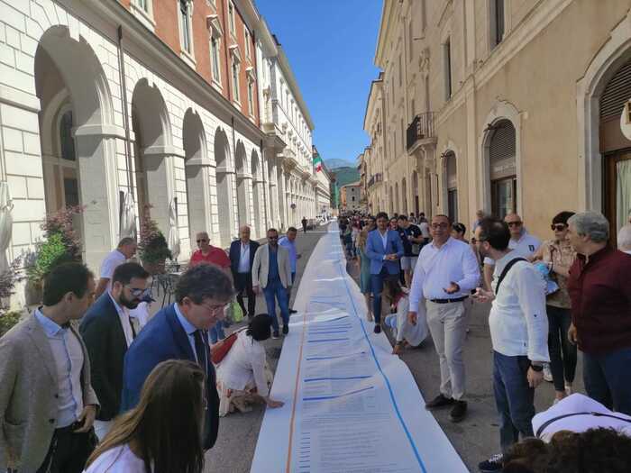 VOTO L’AQUILA: FLASH MOB BIONDI, ROTOLO DI 200 METRI CON PROGRAMMA DI MANDATO LUNGO IL CORSO
